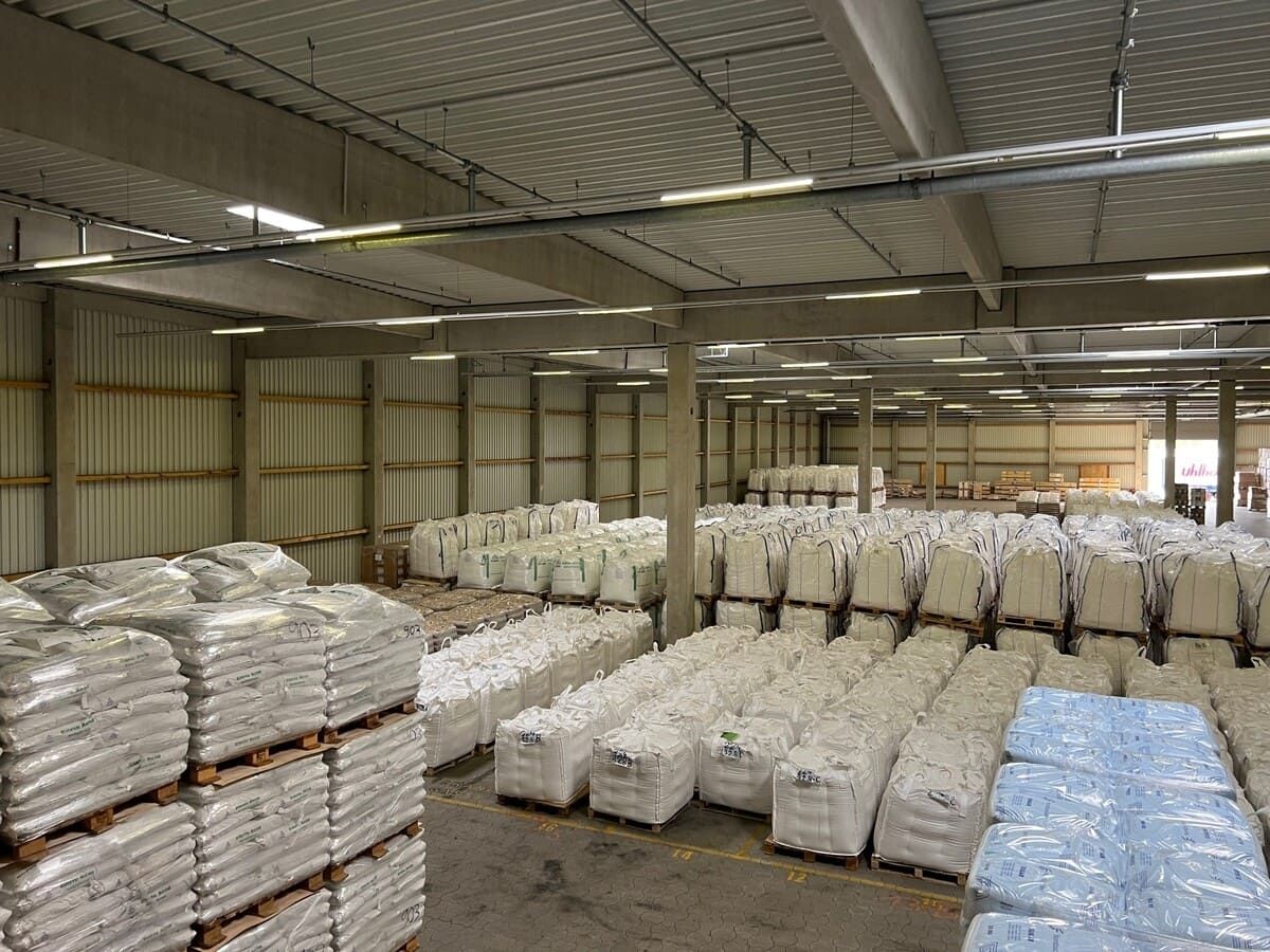 A spacious warehouse filled with stacked white bags on pallets, organized for storage and distribution, under industrial lighting.